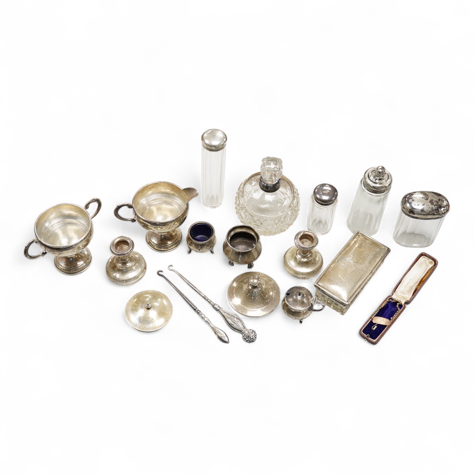 An early 20th century silver mounted cut glass scent bottle, five silver mounted glass toilet jars, a pair of silver mounted dwarf candlesticks, two silver condiments, a sterling jug(weighted), a sterling cup and cover(w